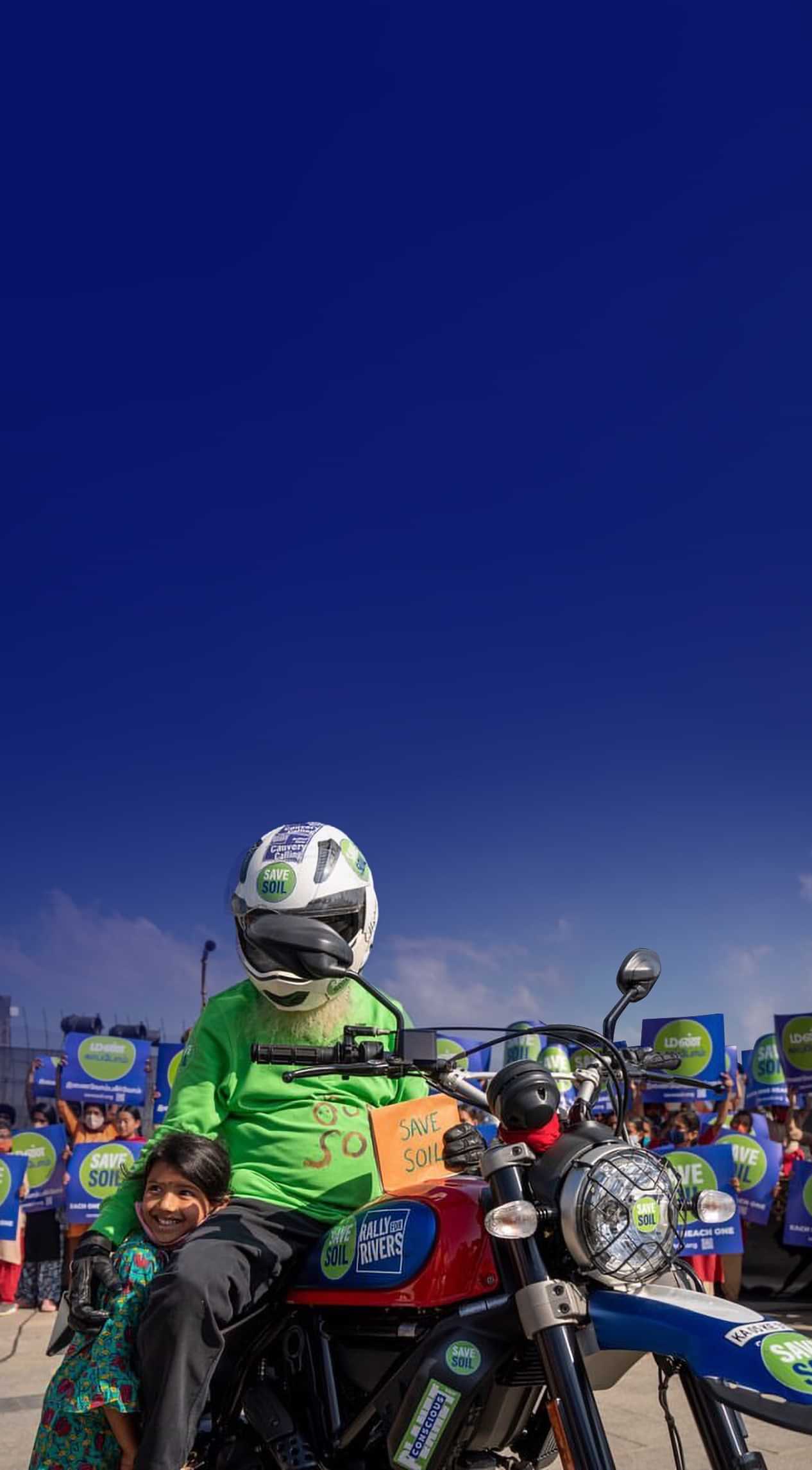 Sadhguru on motorcycle with Save Soil sign, alongside child