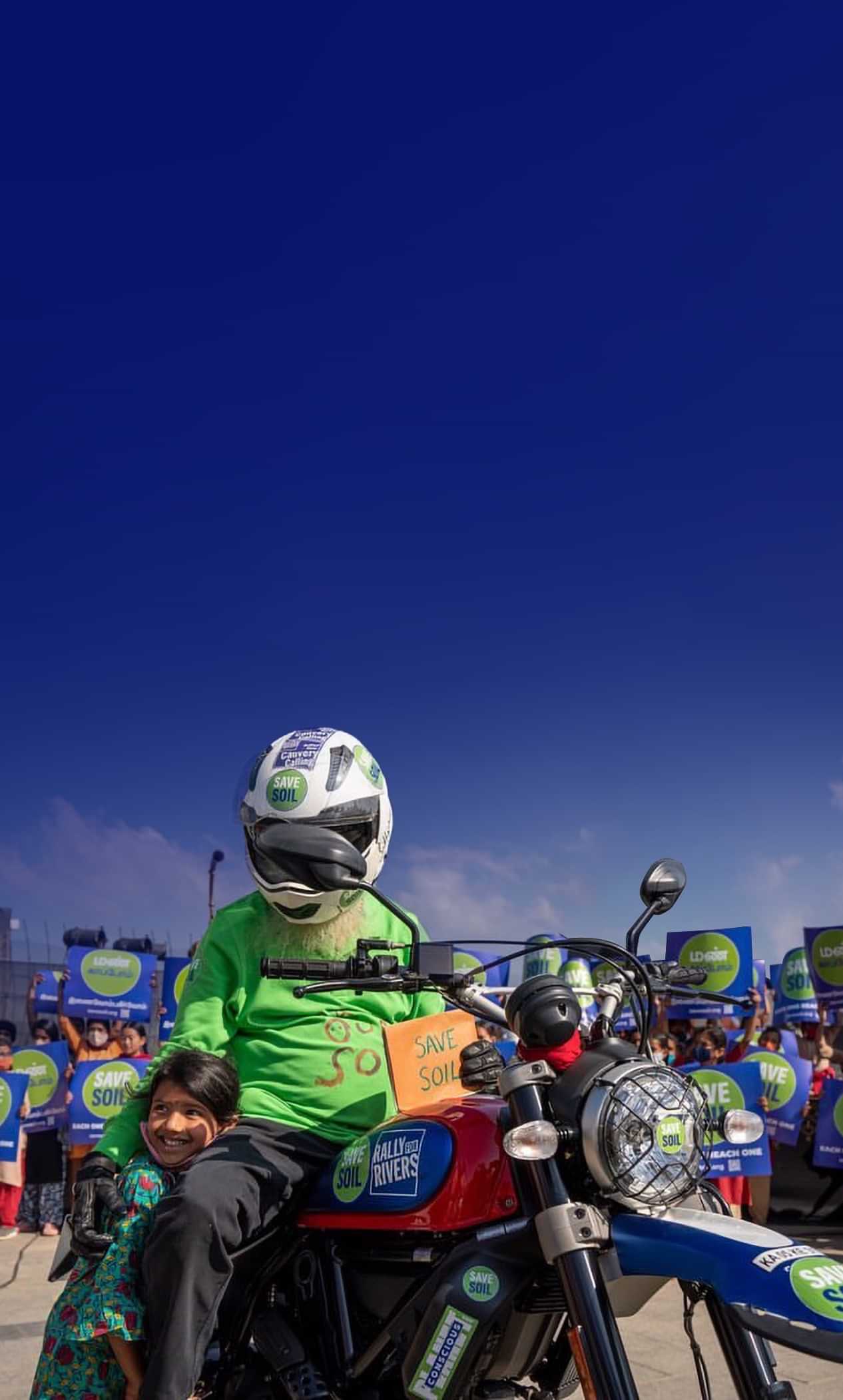 Sadhguru on motorcycle with Save Soil sign, alongside child